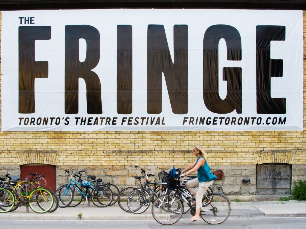 Photo of woman cycling past Toronto Fringe Theatre Festival banner